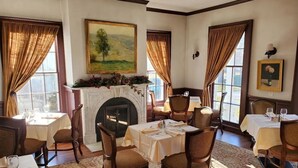 Comedor con chimenea, mesas de comedor, sillas y ventanas amplias con cortinas.