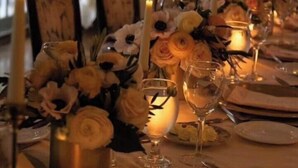 Una mesa dispuesta para comer, con velas, copas y un centro de mesa floral.