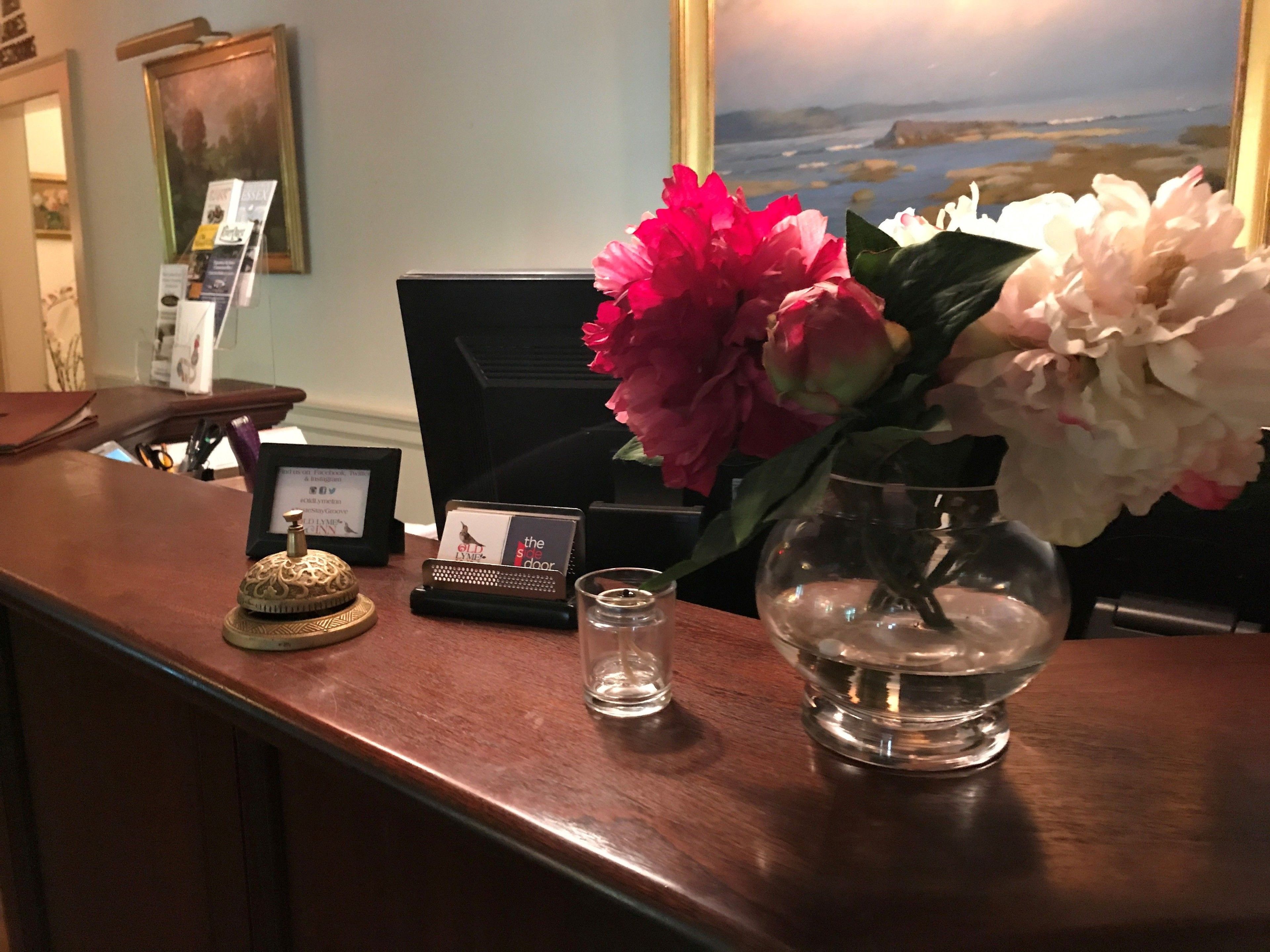 A reception desk with a vase of flowers, a small decorative item, a card holder, and a framed picture on the wall.