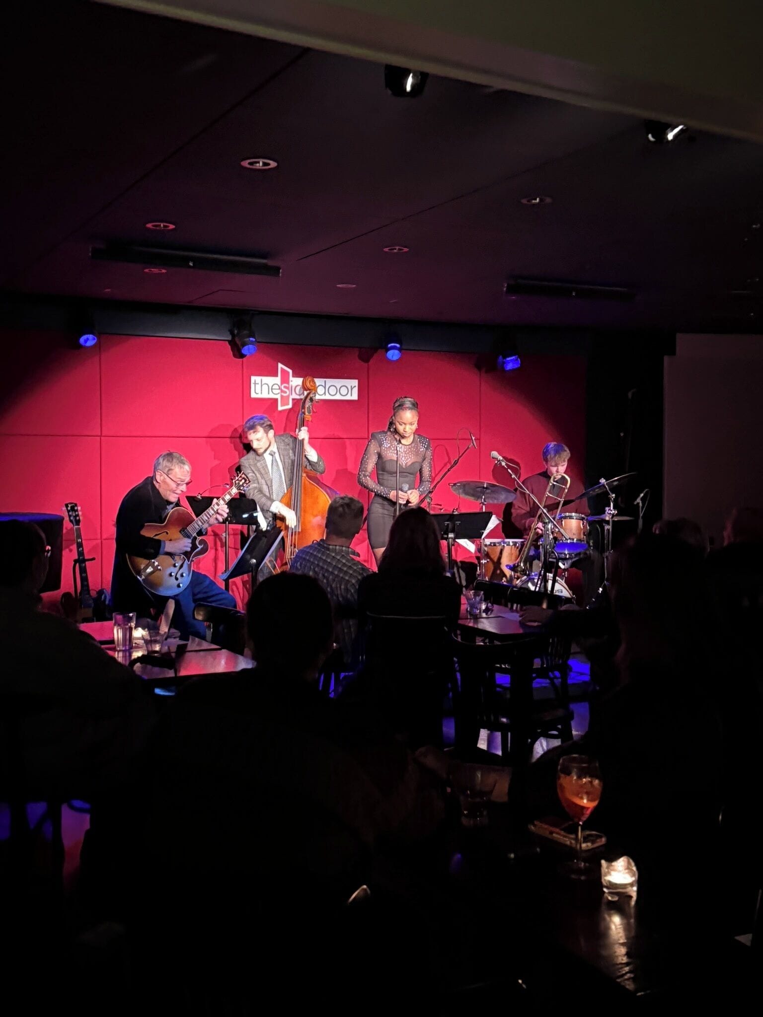 A band performing on a stage with a red backdrop and a cross symbol.