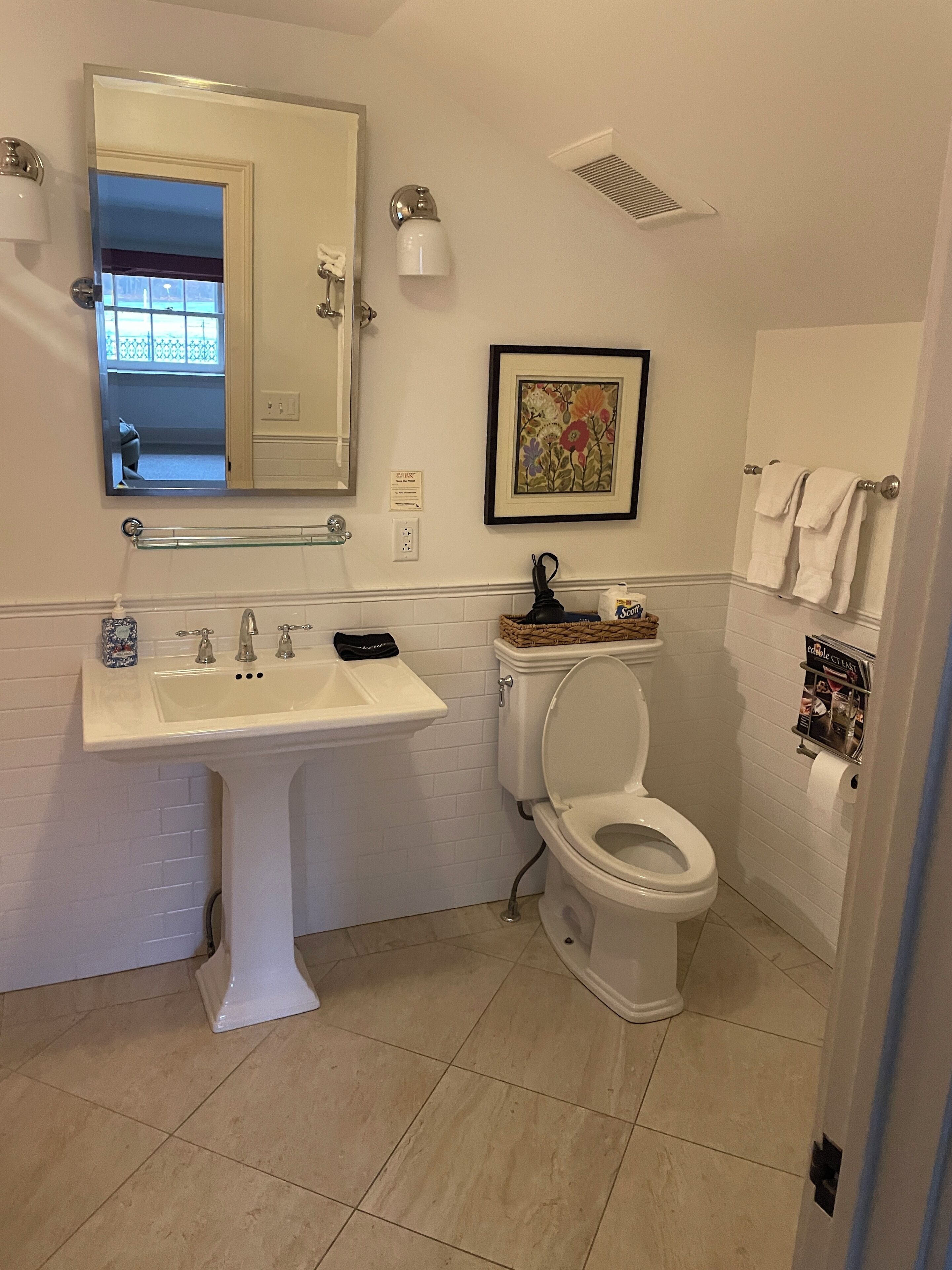 Un baño con lavamanos pedestal, inodoro y un cuadro con flores en la pared.