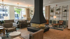 A modern living room with a large fireplace, comfortable seating, and a view of the street. - Six South St Hotel (Hanover)