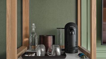 A minibar with a coffee maker, glassware, and a tray with utensils.
