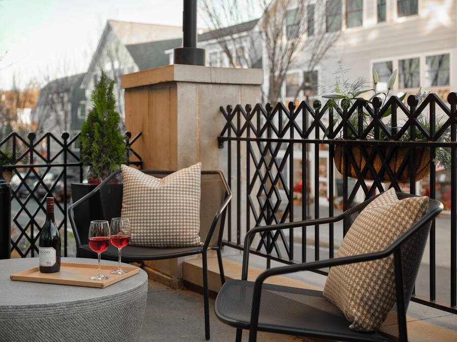 Un espacio al aire libre con sillas de mimbre y una mesa, una botella de vino tinto y una copa sobre la mesa.