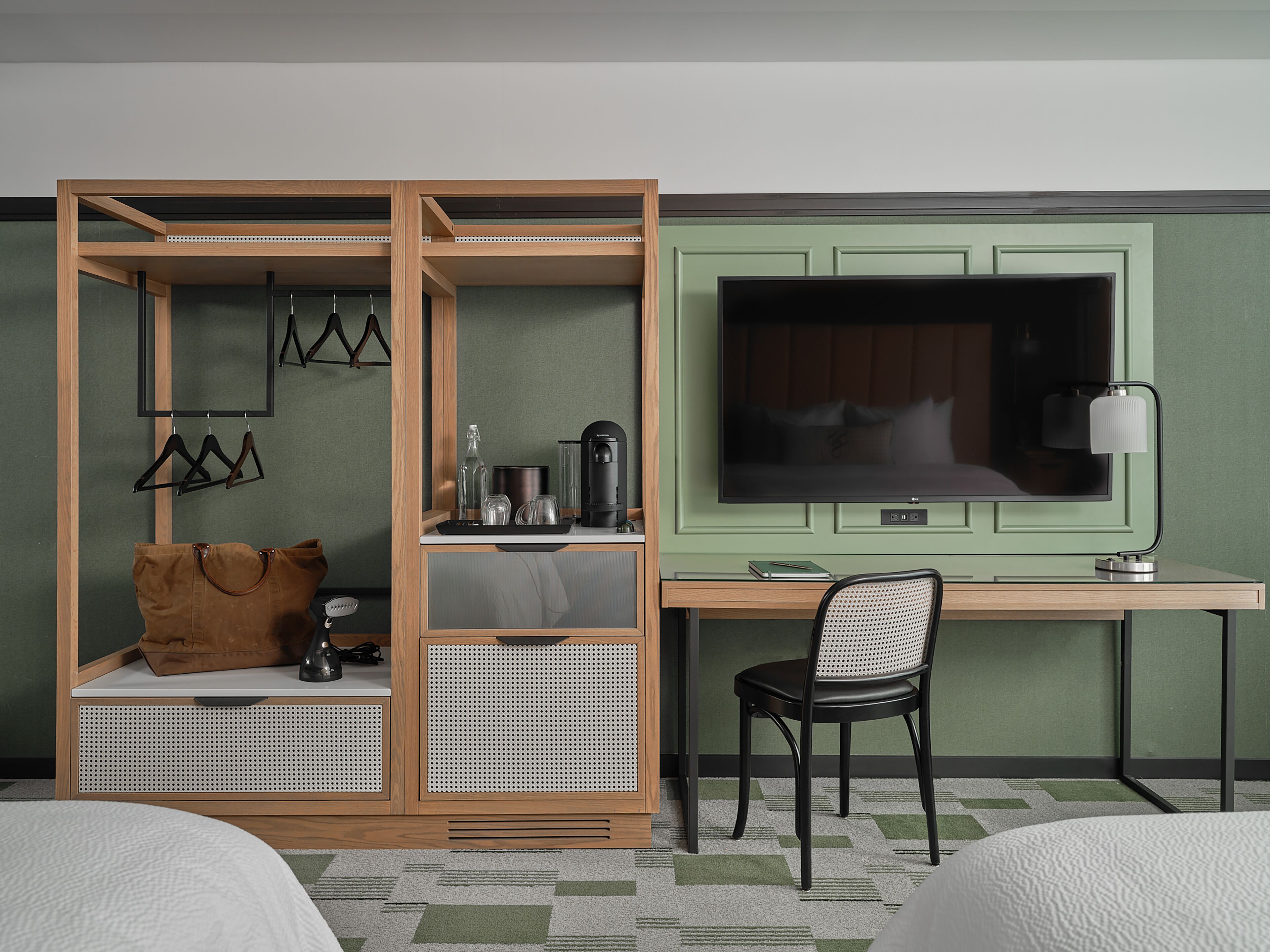 A hotel room with a bed, a desk with a chair, a television, a coffee maker, and a hanging light fixture.