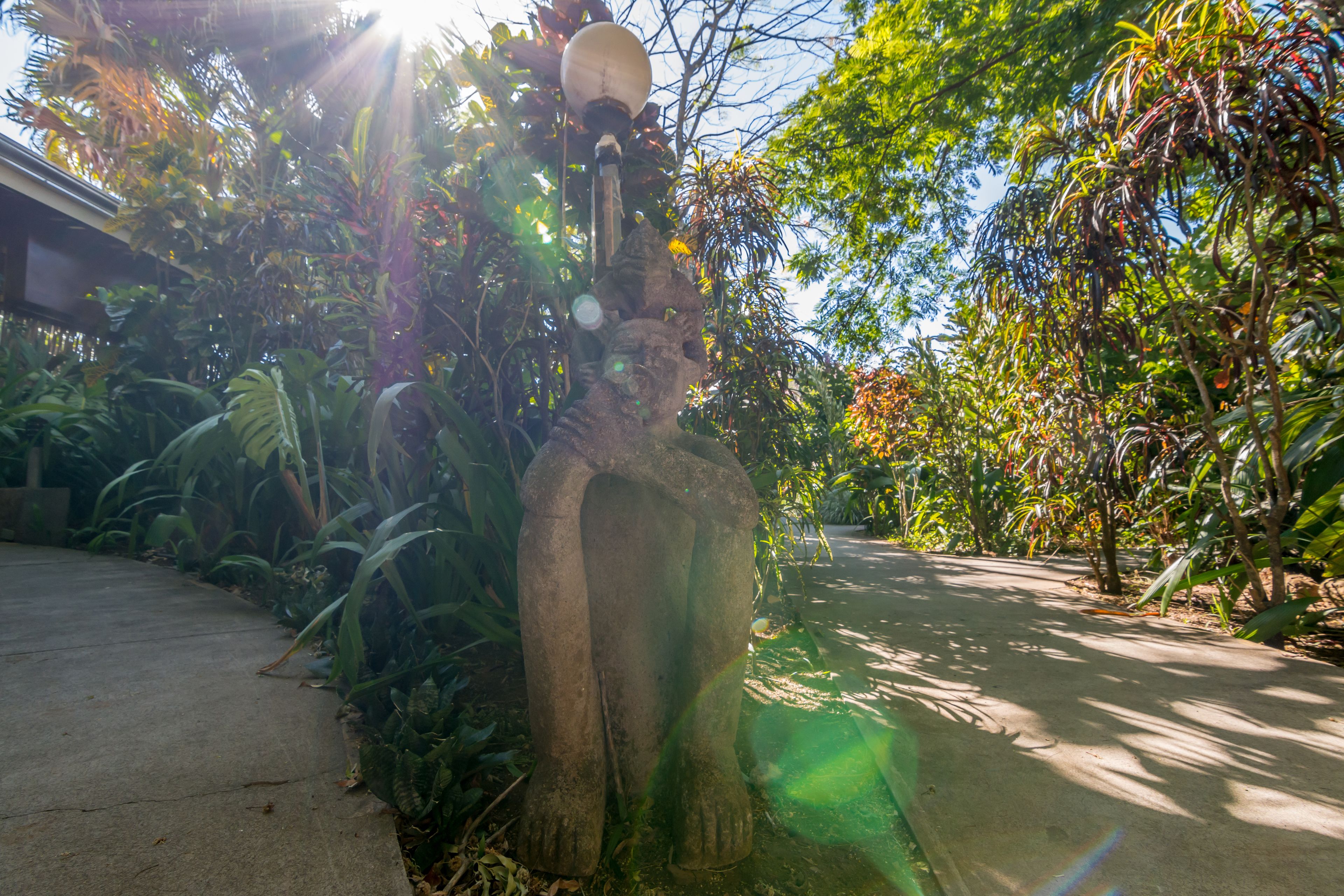 A concrete pathway flanked by lush greenery and a stone sculpture.