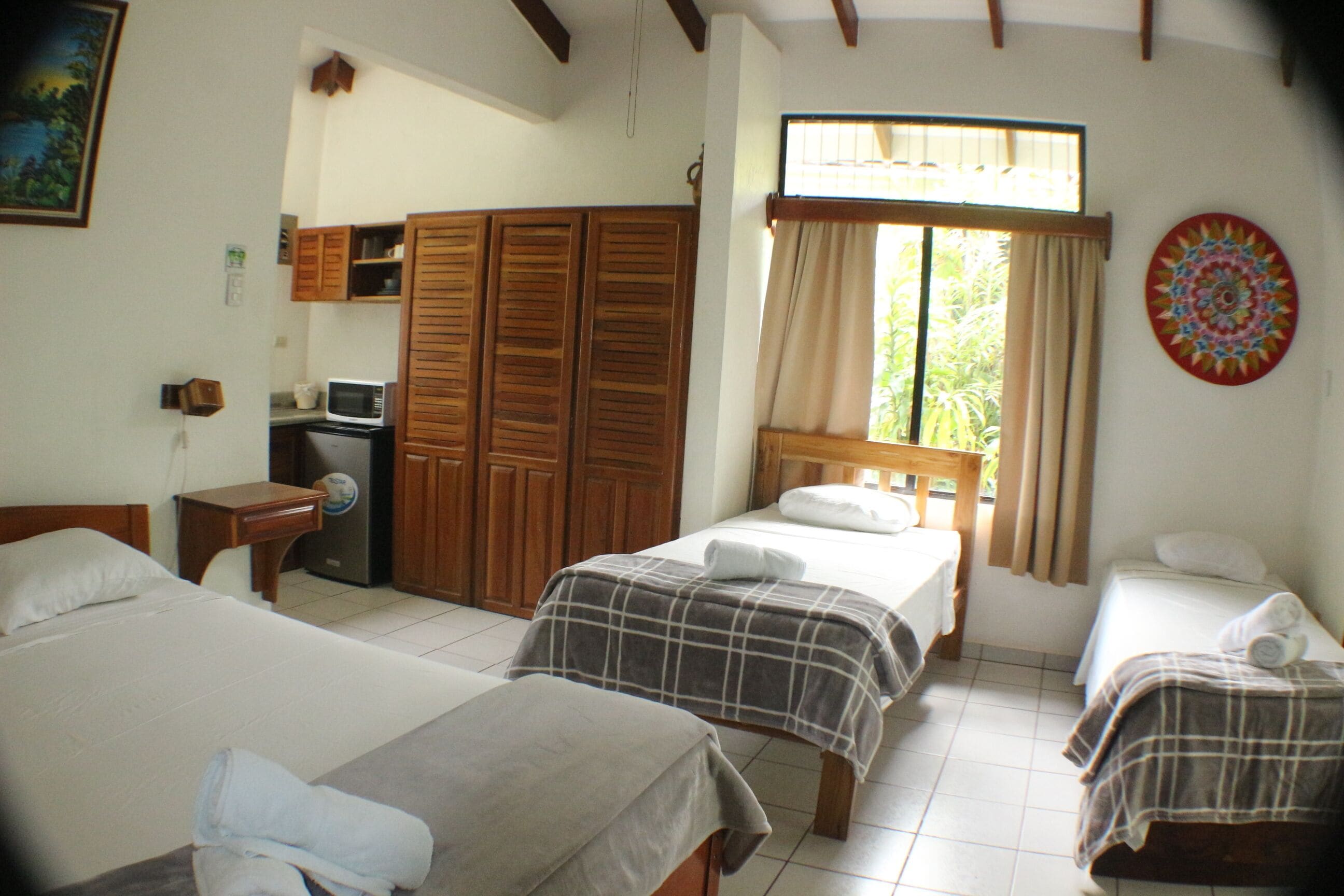 Una habitación con dos camas, un armario, un microondas y un ventanal con cortinas.