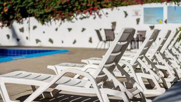 Una fila de sillas de sol blancas junto a una piscina con una pared blanca y una piscina azul al fondo.