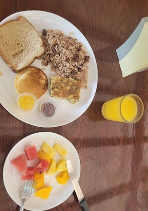 Un plato de desayuno con tostadas, panqueques y arroz, junto a un plato de fruta con sandía y piña.
