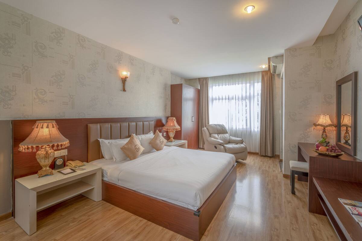 A hotel room with a large bed, bedside lamps, a desk with a lamp, a chair, and a mirror.