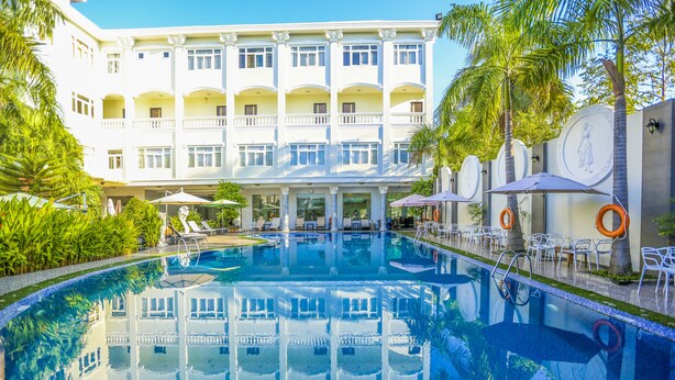 A hotel with a large pool, outdoor seating, and a white building with balconies. - Eden Plaza Danang (Da Nang)
