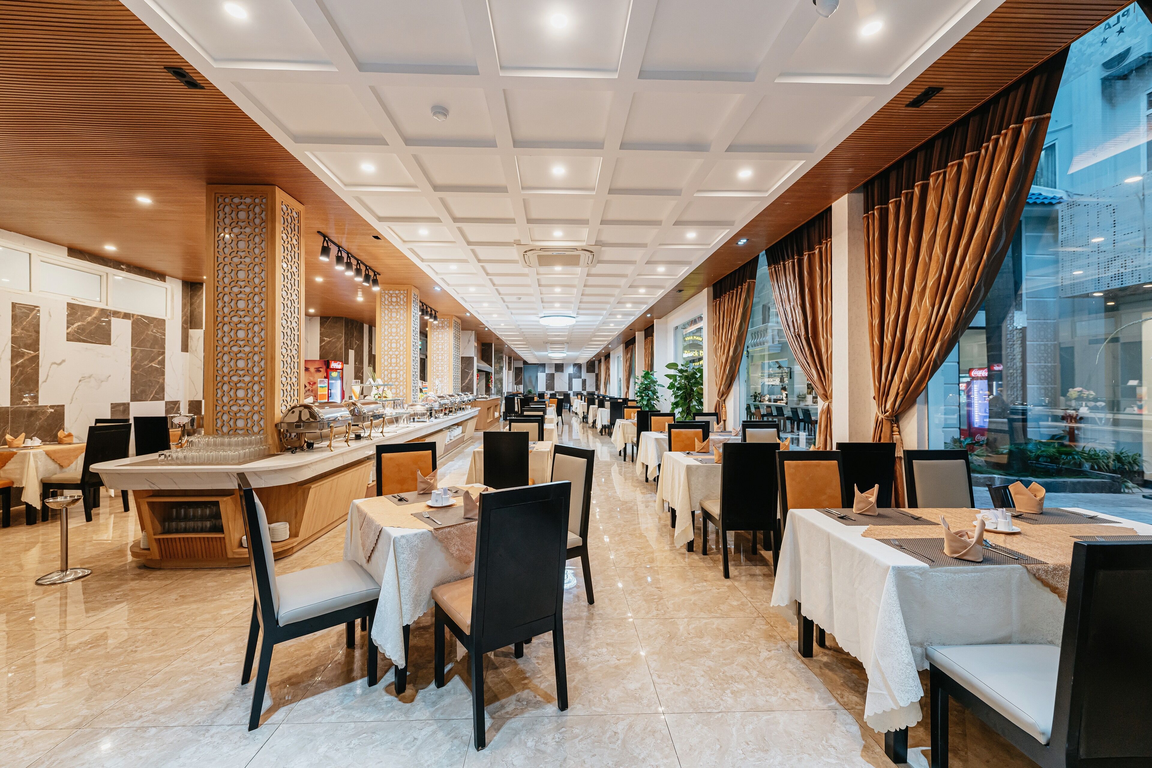 Un restaurant espaiós amb moltes taules i caires, una zona de bar central i grans finestres que donen vistes al carrer.