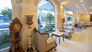 A spacious lobby with a grand chandelier, elegant furniture, and a large arched window offering a view of the street. - Eden Plaza Danang (Da Nang)