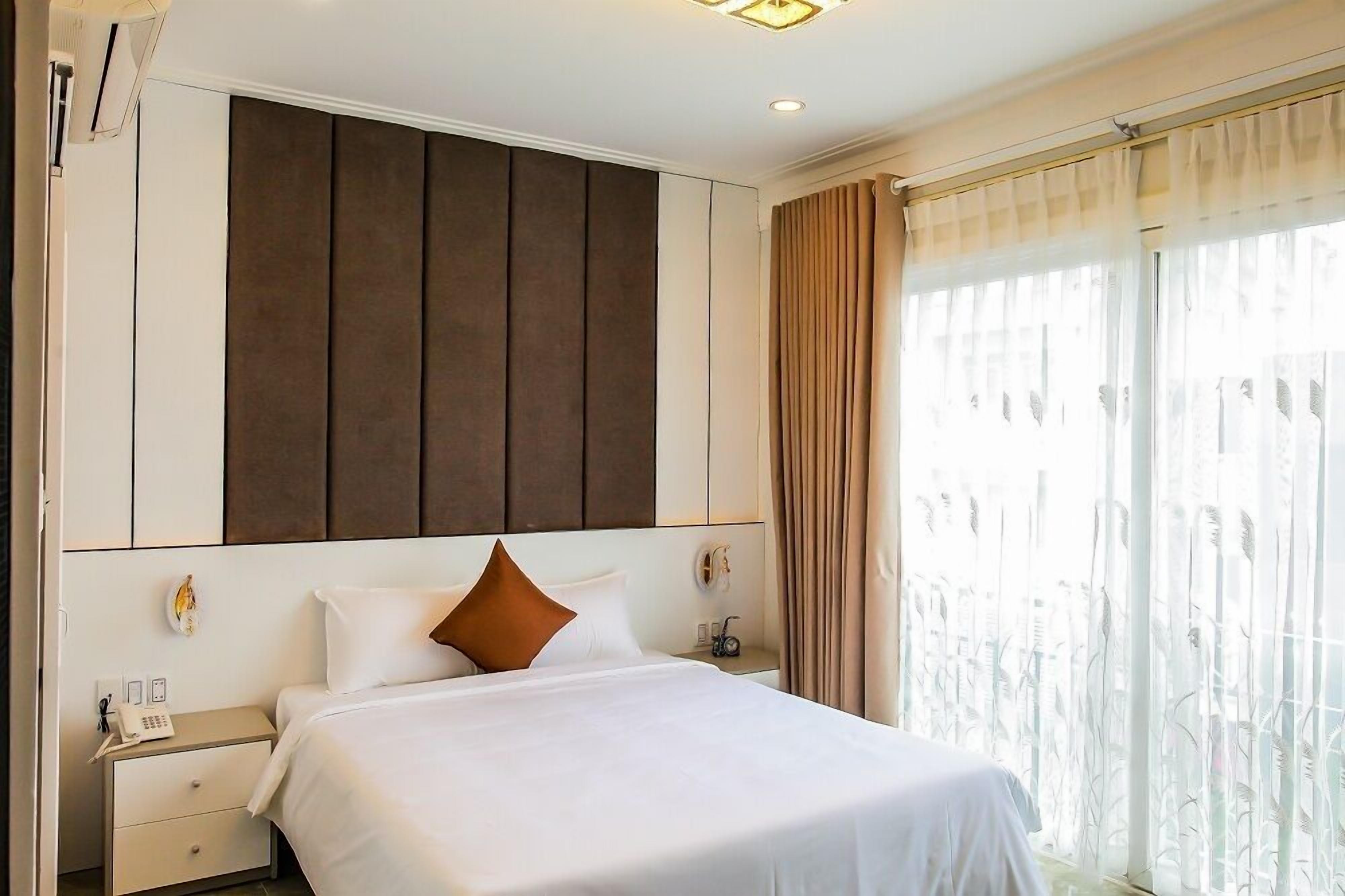 A hotel room with a large bed, a nightstand, a telephone, and a window with curtains.
