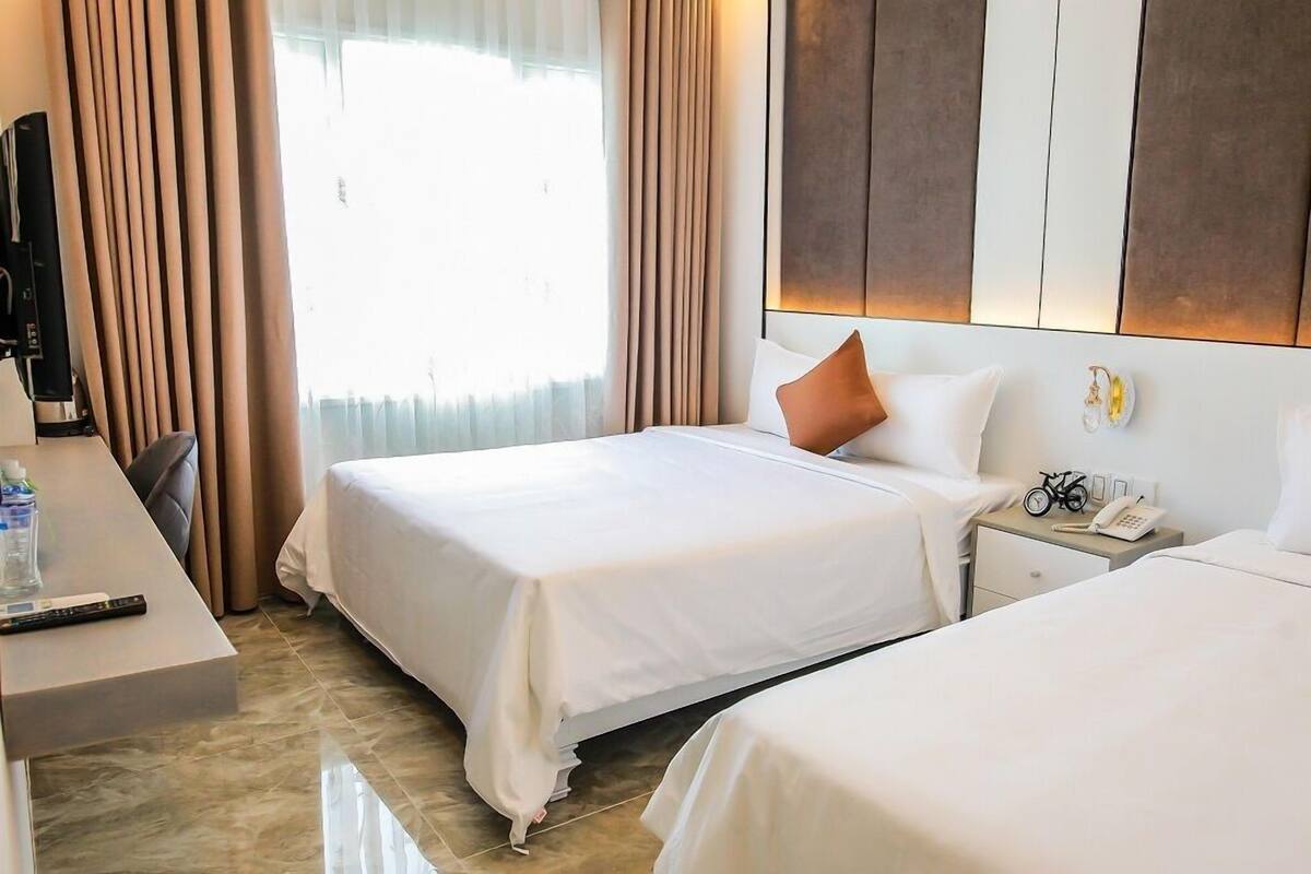 A hotel room with two beds, a desk with a chair, a TV, and a bedside table with a phone and a bicycle decoration.