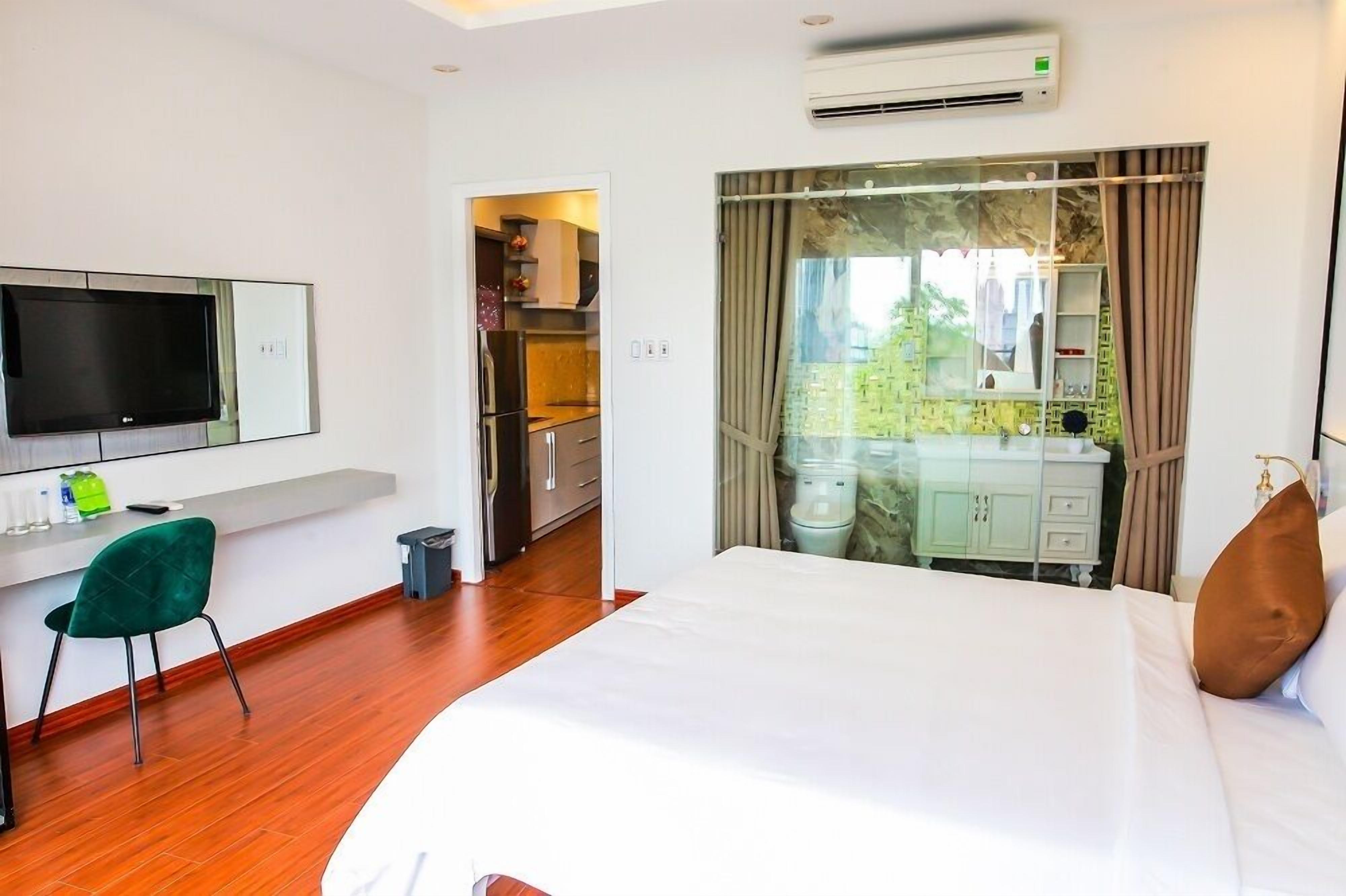 A hotel room with a bed, a desk with a chair, a TV, and a bathroom with a mirror and sink.