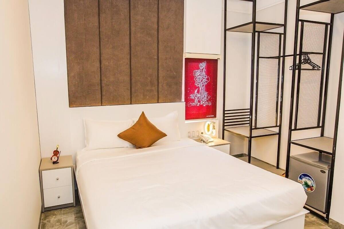 A hotel room with a bed, a nightstand, a wardrobe, and a small refrigerator.