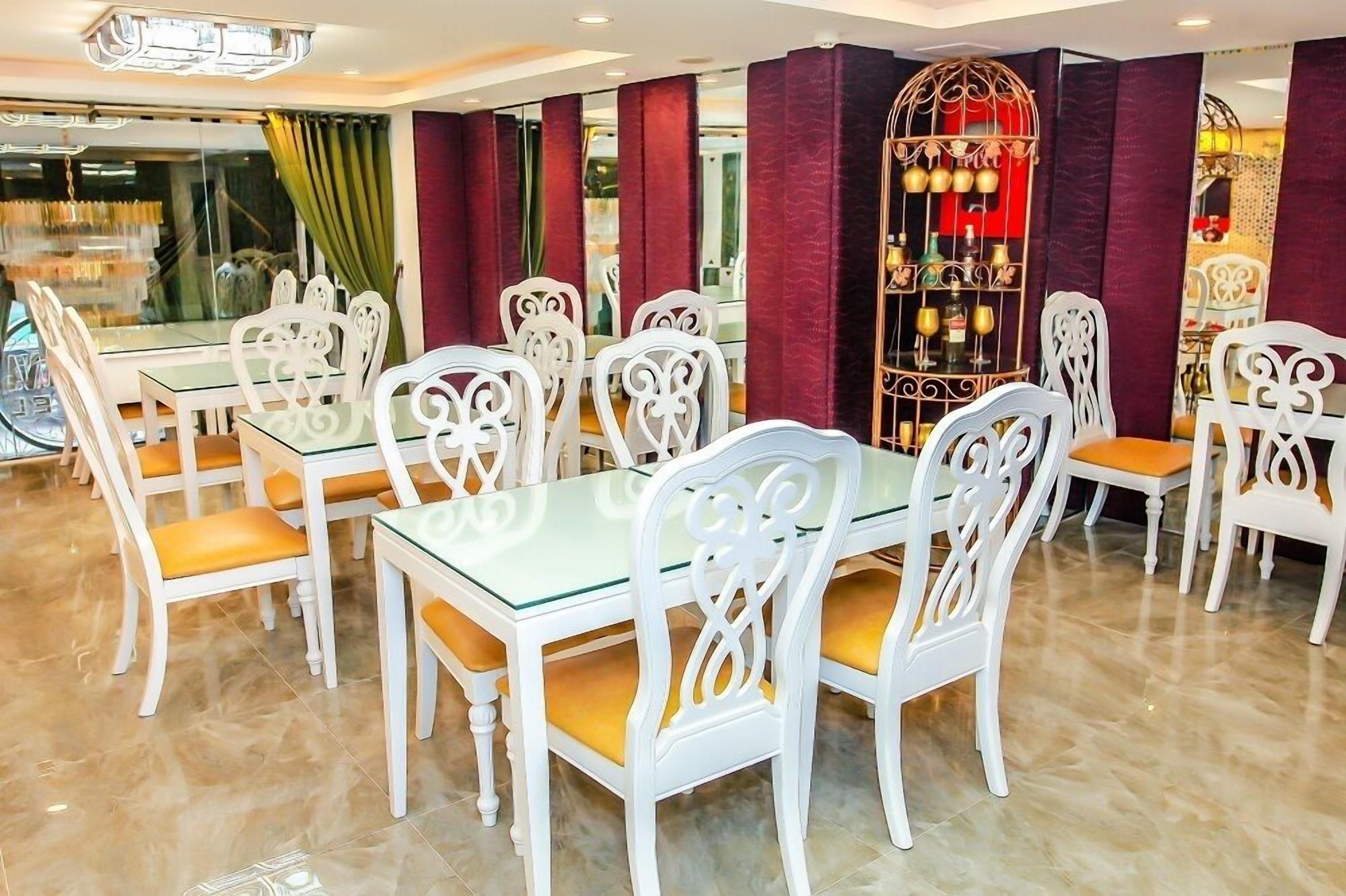 A dining area with white chairs and glass tables, red curtains, and a decorative metal shelf with bottles.
