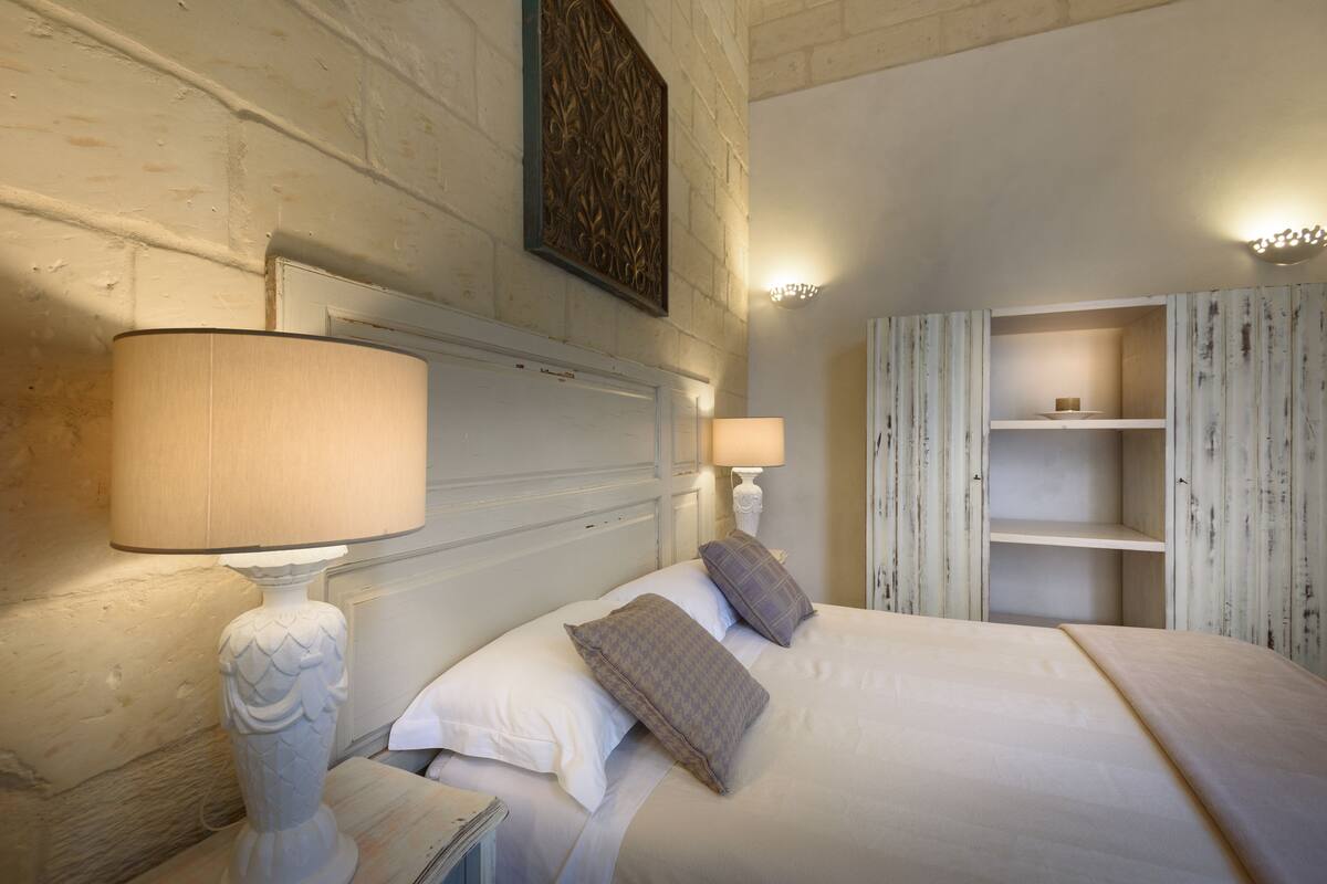 A neatly arranged bedroom with a large bed, two bedside lamps, and a wardrobe with open shelves.