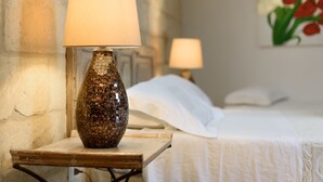 Un lit avec du linge de lit blanc et une table de chevet surmontée d’une lampe à motifs de mosaïque.