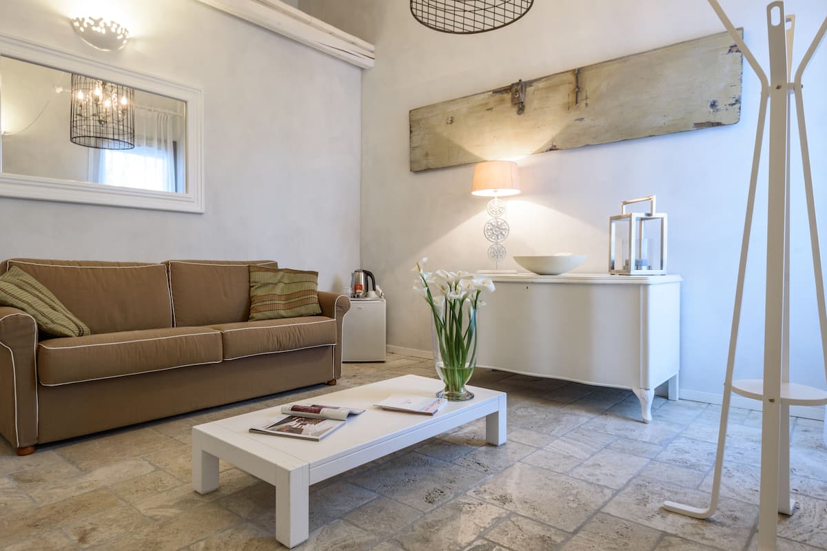 A living room with a brown sofa, a white coffee table, a lamp, and a white side table with a bowl.