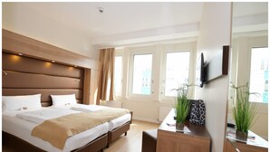 Ein modernes Hotelzimmer mit einem großen Bett, einem hölzernen Kopfteil, einem Schreibtisch mit Spiegel und einem an der Wand befestigten Fernseher.