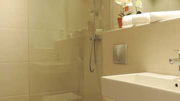 A modern bathroom with a glass-enclosed shower, a white toilet, and a sink with a mirror above it.