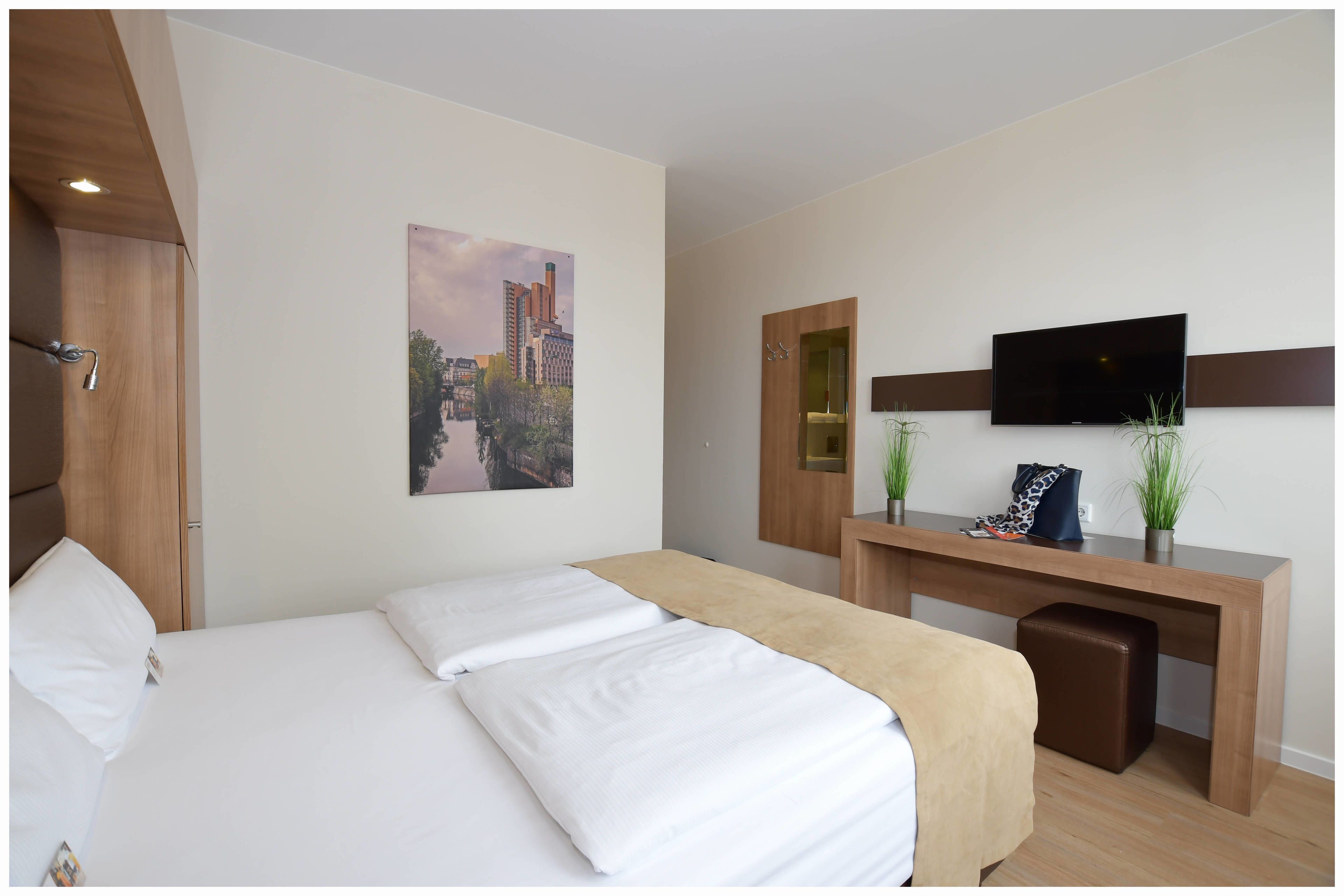 Een hotelkamer met een bed, een bureau, een televisie en een stadsgezicht op een schilderij.