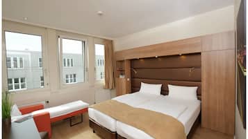 A modern hotel room with a large bed, a bench, and a desk.