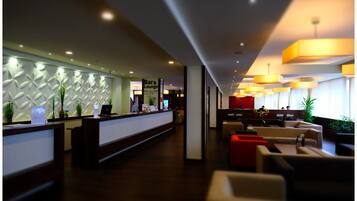 Un hall de hotel con mostrador de recepción, zona de bar/salón y arreglos de asientos.