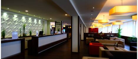 A hotel lobby with a reception desk, a bar/lounge area, and seating arrangements.