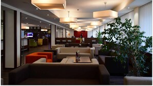 Eine moderne Hotelhalle mit mehreren Sitzbereichen, einem Fernseher und einer großen Pflanze.