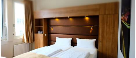 Una habitación de hotel con una cama grande, cabecero de madera y una ventana con cortinas.