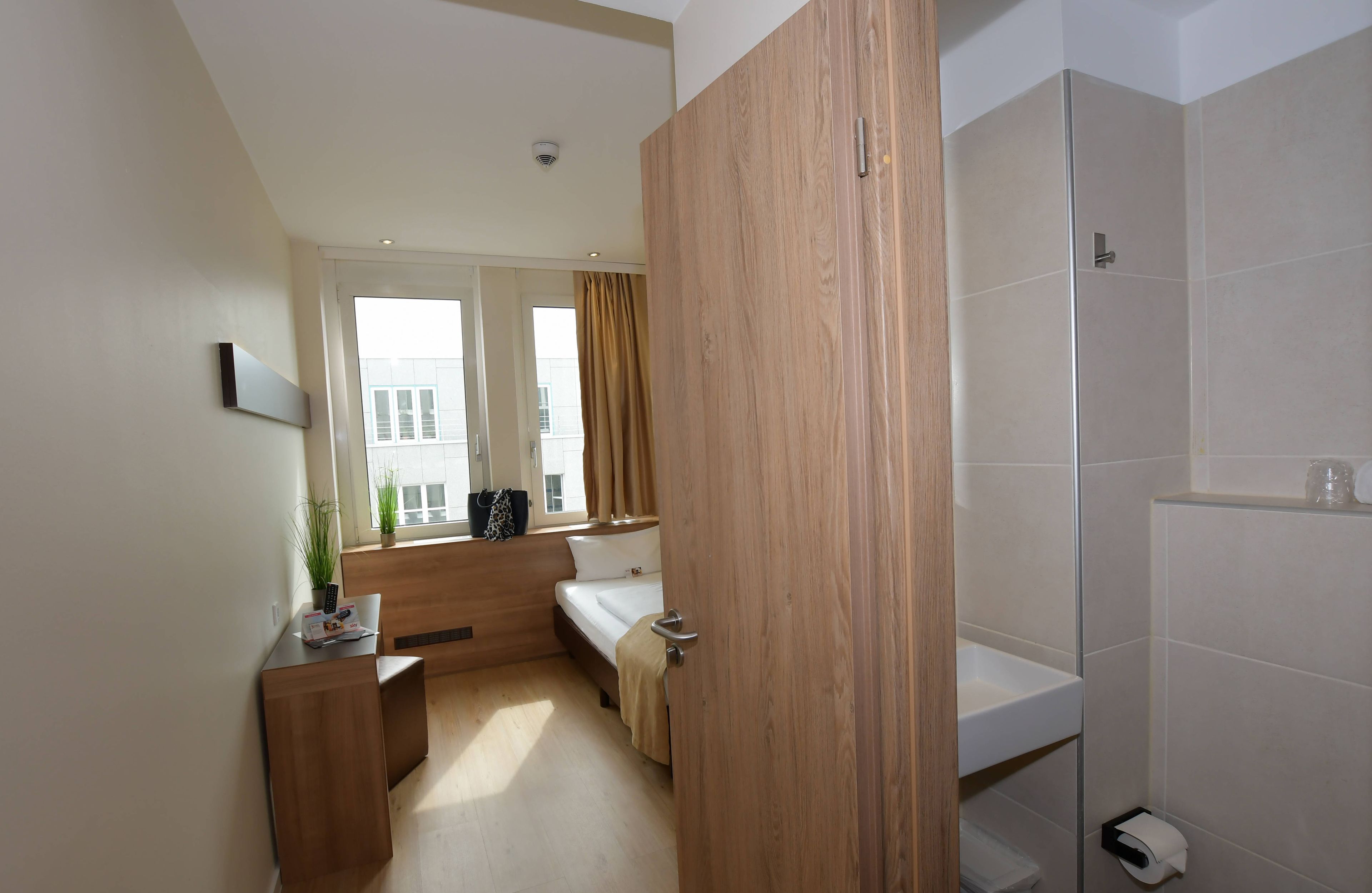 A modern hotel room with a bed, bedside table, and a window with curtains.