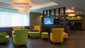 Eine Lobby mit grünen und gelben Sesseln, einem Flachbildfernseher und Holzböden.