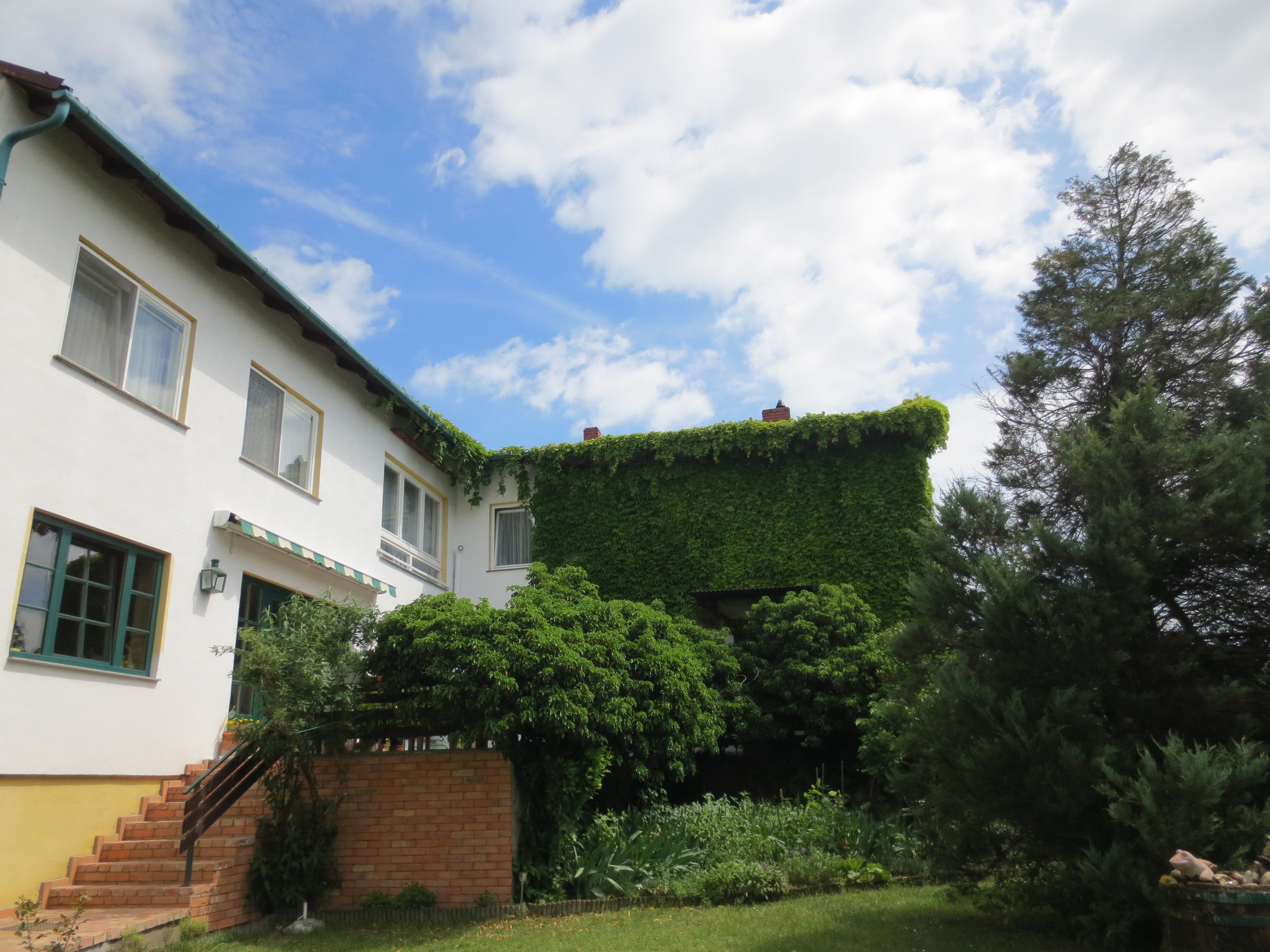 A two-story building with a white facade, green window frames, and a brick staircase leading to the entrance.