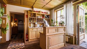 A wooden interior with a central counter, shelves with bottles, and a view of greenery outside. - Wein & Landhaus Willi Opitz (Illmitz)