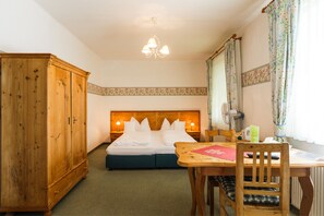 A bedroom with a wooden bed, a wooden wardrobe, a dining table with a chair, and a chandelier. - Wein & Landhaus Willi Opitz (Illmitz)