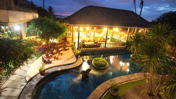 A pool area with a lounge, palm trees, and a building with a thatched roof. - Sanur Seaview Hotel (Denpasar)