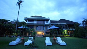 A large house with a well-maintained lawn, outdoor seating area with lounge chairs and umbrellas, and a visible staircase leading to the entrance. - Sanur Seaview Hotel (Denpasar)