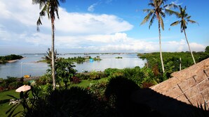 A tropical landscape with palm trees, a body of water, and a distant city skyline. - Sanur Seaview Hotel (Denpasar)