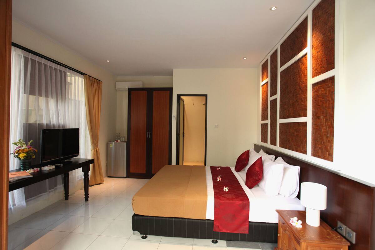 A hotel room with a bed, a TV on a desk, a wardrobe, and a bathroom door.