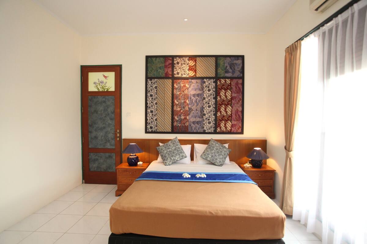 A bedroom with a large bed, two nightstands, a wall art piece, and a door.