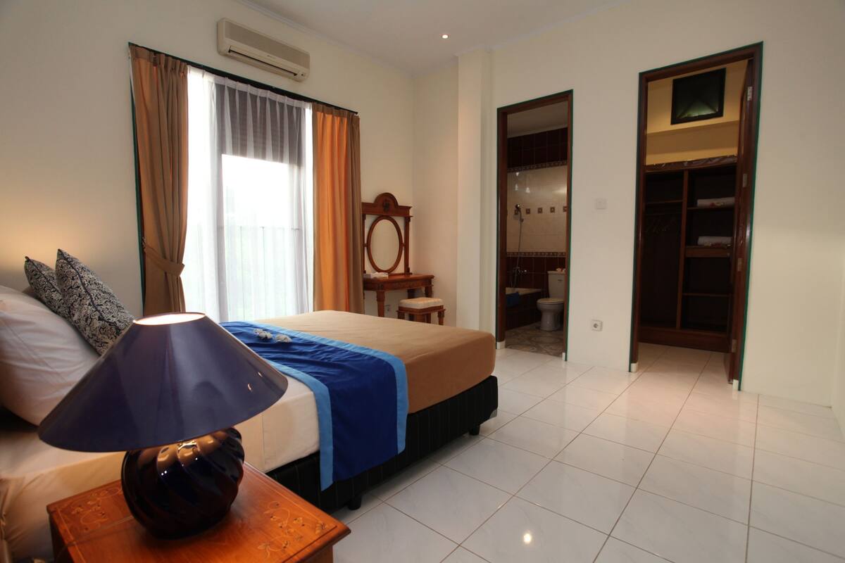 A hotel room with a bed, a bedside lamp, a mirror, a small table, and a wardrobe.