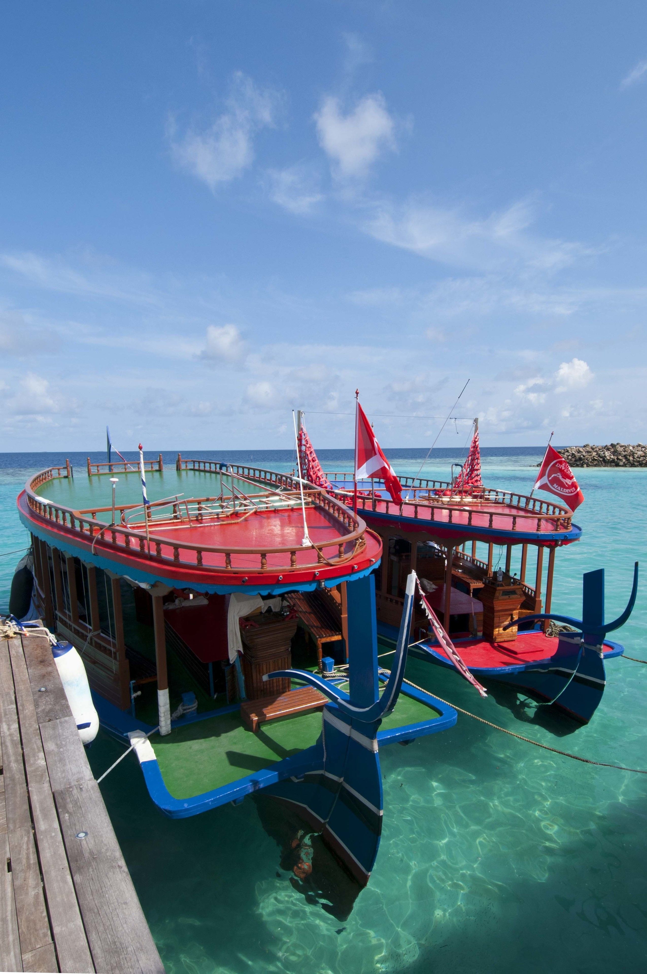 Ein Boot mit blauer und roter Deckfläche, zwei roten Flaggen und einem wolkenlosen, blauen Himmel.