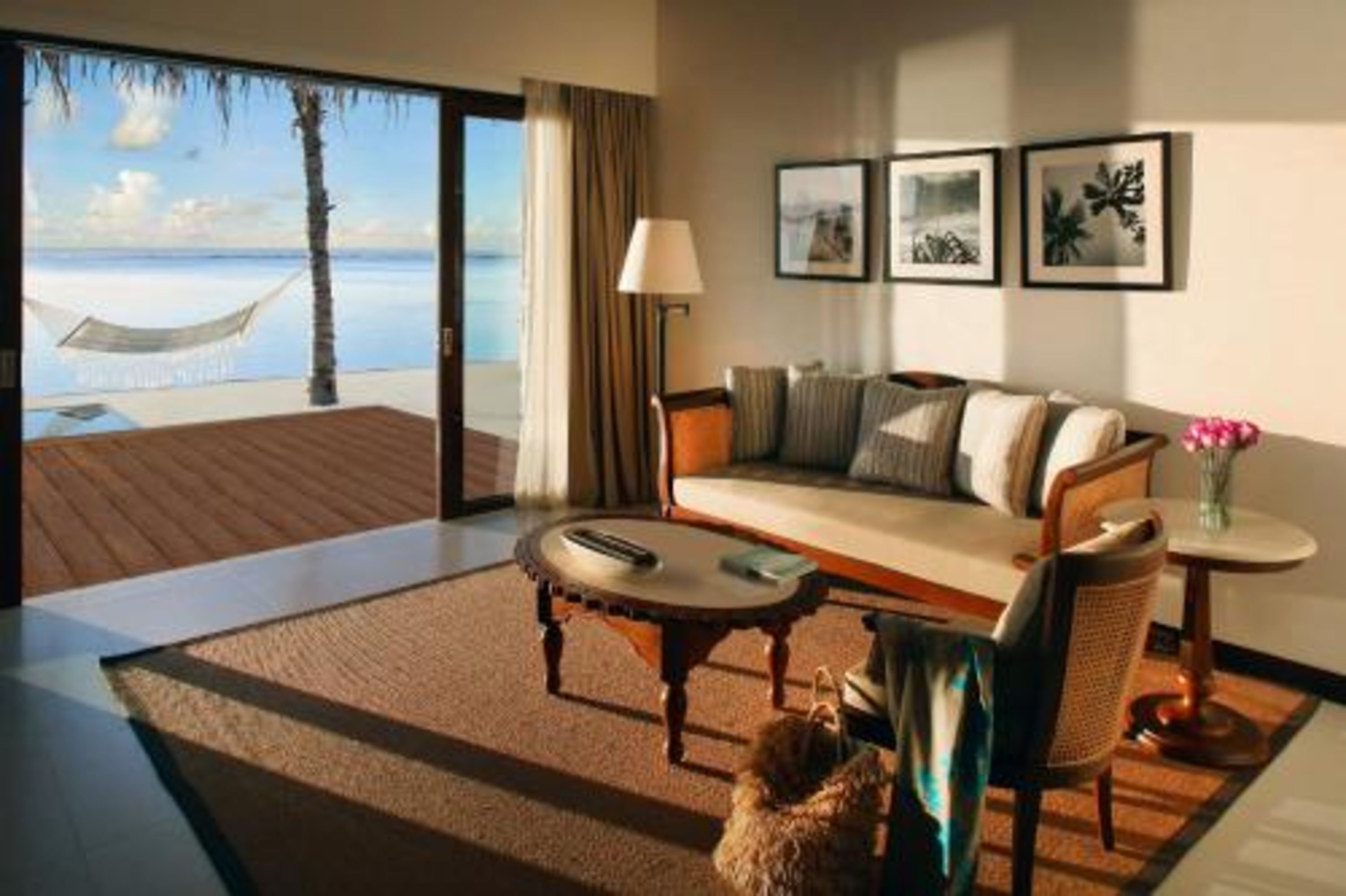 A hotel room with a sofa, a small round table, a lamp, and a view of the beach through a glass door.