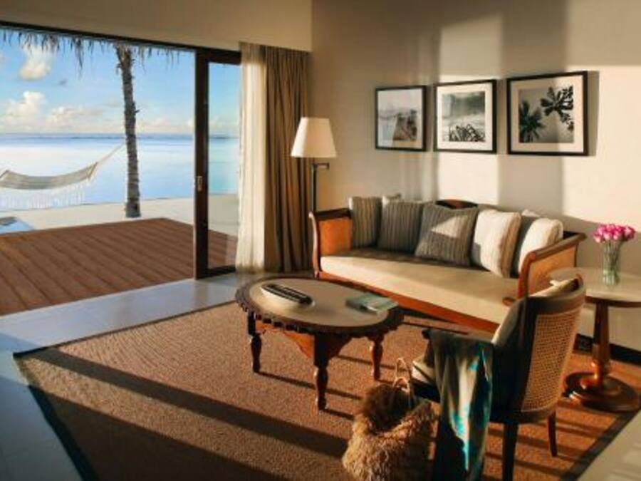 A hotel room with a sofa, a small round table, a lamp, and a view of the beach through a glass door.