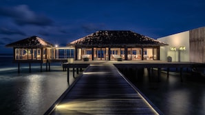 Un resort frente al agua con bungalows sobre el agua unidos por una pasarela de madera.
