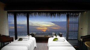 Una habitación con dos camas y vistas al océano, con un atardecer.