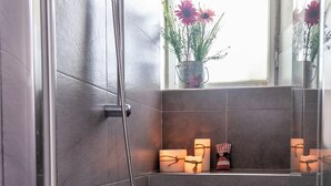 A shower with a handheld showerhead and a wall-mounted faucet. There is a window above the shower, and a small shelf with candles and a figurine. - La Colonna ( Historic Center ) (Lucca)